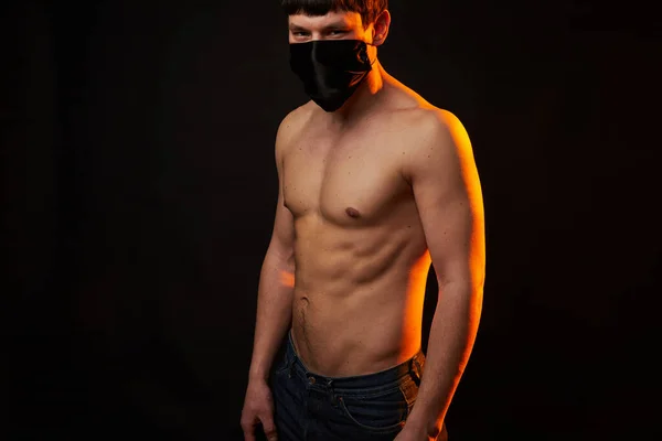 muscular young guy in black medical mask on black background