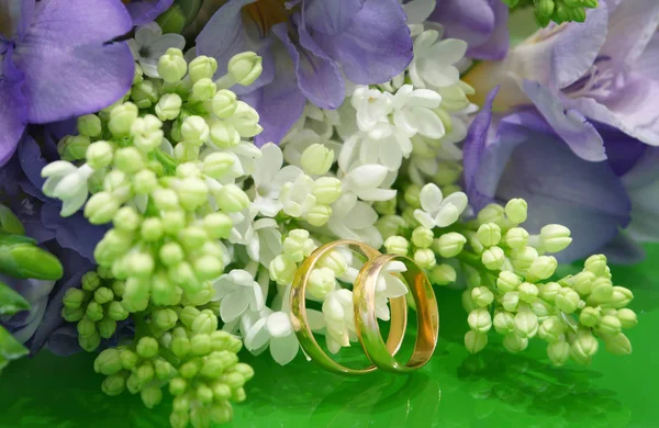Two wedding rings and a wedding bouquet of white lilac and purple freesias — Stock Photo, Image