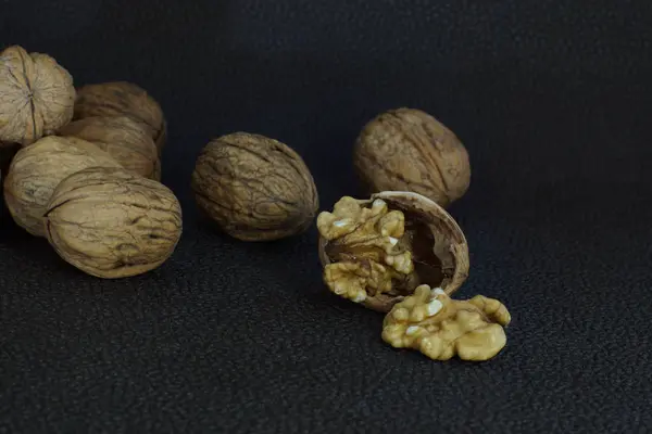 Walnuts lie in a heap on a dark background, one is split, half the shell and a kernel — Stock Photo, Image