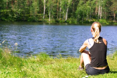 Bir kız yaz aylarında göl kıyısında oturur ve doğa hayran