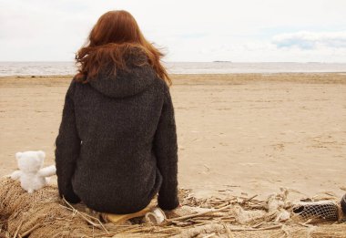 Kız Balık ağı üzerinde oturur ve körfezin yanındaki sırtında bir oyuncak ayı su bakar