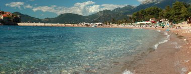 Yatay bir panorama bir plaj ve bir sürü insan bir dinlenme ile defne deniz manzaralı. Temiz su, dağlar ve bulutlu bir gökyüzü uzaktan temizleyin