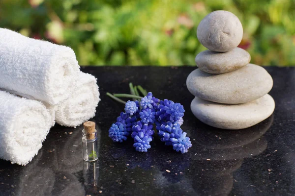 Set para procedimientos de spa, piedras de masaje, toallas de rizo blanco y flores azules Mischures en una mesa de granito pulido en el jardín — Foto de Stock