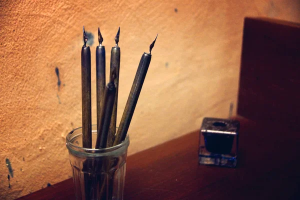 Antiche penne di piume sul tavolo vicino al calamaio, tracce di macchie sul muro — Foto Stock