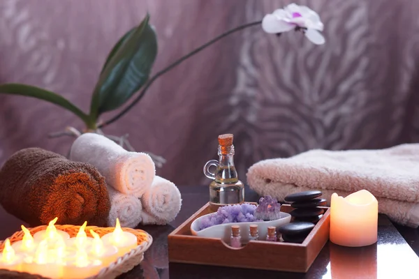 Set pour soins spa avec bougies électriques et serviettes éponge. Dans une boîte en bois, huile et pierres pour massage, sel violet et améthyste, une orchidée en arrière-plan — Photo