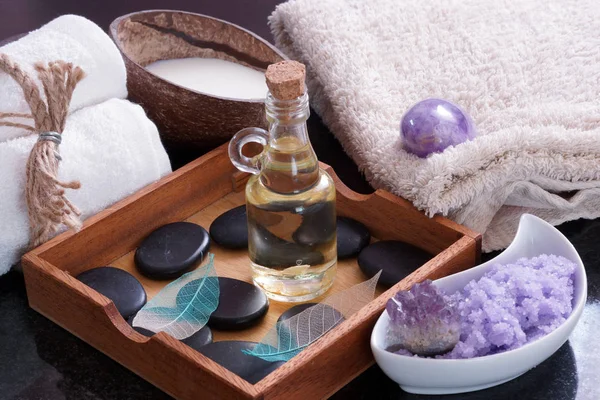 Aromatisk olja med varma stenar för massage i en trälåda bredvid handdukar, lila salt och mjölk i en kokosnöt. — Stockfoto