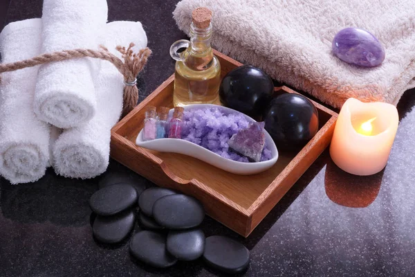 Białe ręczniki podłączony przez sznurka obok zestaw do masażu z Bian kamienie, olejki aromatyczne i fioletowy soli, w pobliżu kamienie do masażu hot spa. — Zdjęcie stockowe
