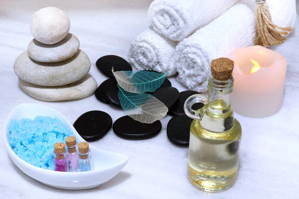 Auf einem Tisch aus weißem Marmor gibt es ein aromatisches Öl, Steine und Salz für die Massage, weiche Handtücher in Rollen und eine sichere elektrische Kerze. — Stockfoto