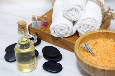Aromatik yağlar, yumuşak havlular, sıcak taşlar ve banyo tuzu bir kaşık beyaz mermer masada ahşap bir kasede Spa yordamlar kümesi.