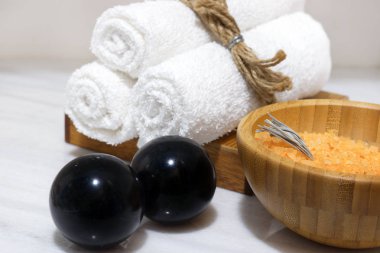 Turuncu banyo tuzu bir ahşap kase ve üç beyaz havlu bir ahşap stand ve siyah Bian taşlar beyaz mermer tablo üzerinde durmak