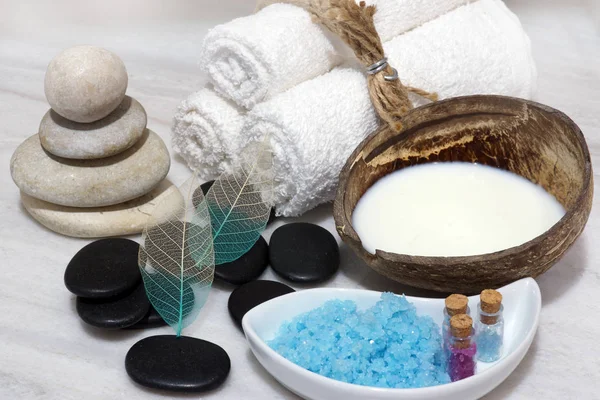 Ett set för spabehandlingar med kokosmjölk föryngrande mjölk, stenar och blå badsalt ligger på den vita marmor bänkskivan. — Stockfoto