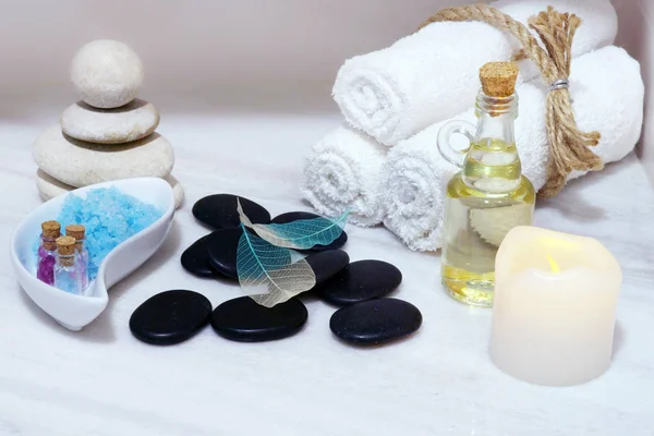 Conjunto para procedimientos de spa en una mesa de mármol blanco: aceite aromático, piedras para masajes calientes, sal de baño azul y toallas, atadas con cuerda . —  Fotos de Stock