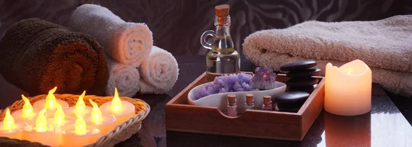 Conjunto para tratamentos de spa com velas eléctricas e toalhas terry. Em uma caixa de madeira óleo e pedras para massagem, sal roxo e ametista, um conjunto de sal multicolorido em frascos . — Fotografia de Stock