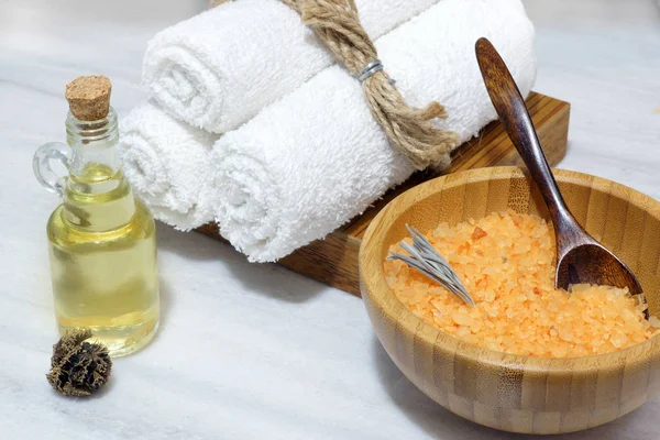 Spa prosedürü - turuncu banyo tuzu bir ahşap kase ve kaşık, üç beyaz havlu bir ahşap kutu ve aromatik yağı masaj bir beyaz mermer tablo için bir şişe için hazırlık
