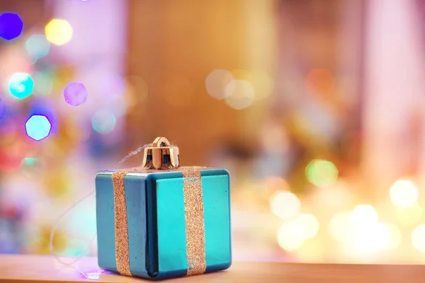 Новорічна листівка з іграшкою у вигляді подарунка зі стрічкою на фоні розмитих вогнів ялинки — стокове фото