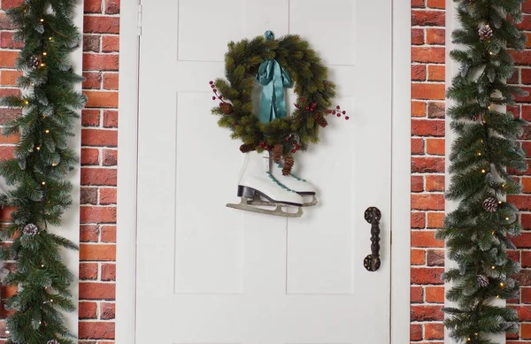 Weiße Schlittschuhe hängen an einem Fichtenkranz. Weihnachtsdekoration der Haustür. — Stockfoto