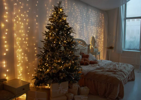 Interior del dormitorio, preparado para el Año Nuevo y decorado con un árbol de Navidad y regalos. Guirnaldas luminosas cuelgan de la pared . — Foto de Stock