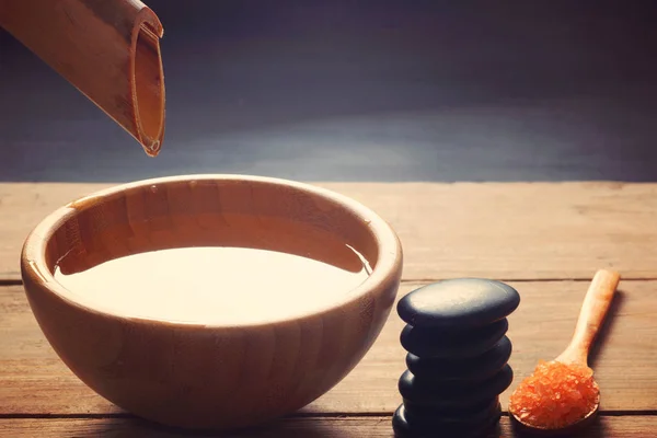 Un conjunto de procedimientos de spa, piedras de masaje caliente, sales de baño y agua con sabor, recogidos de un tallo de bambú en un tazón — Foto de Stock