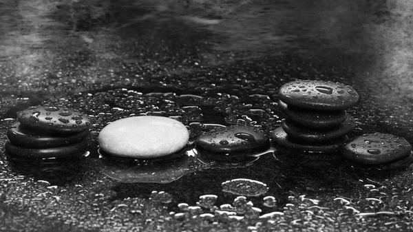 Piedras de spa sobre un fondo oscuro con gotas de agua y reflexión — Foto de Stock