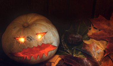 Ahşap arka plan yanındaki Cadılar Bayramı Balkabağı üzerinde sonbahar yaprakları.