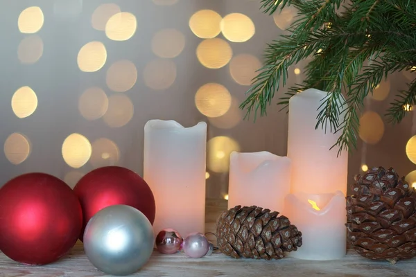 Зажженные свечи, конусы и праздничные шары на фоне рождественской елки и гирлянды — стоковое фото