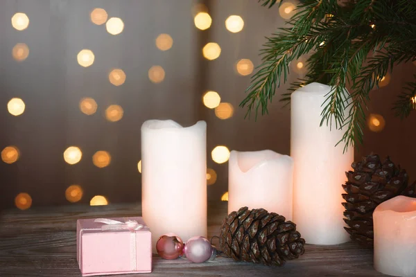 Neujahrsstillleben mit brennenden Kerzen, Beulen und einem Geschenk in einer Schachtel neben einem Weihnachtsbaum und Girlanden im Hintergrund. — Stockfoto