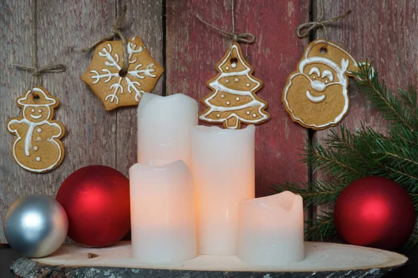 Velas blancas cerca de una pared de madera roja con galletas de Navidad y ramas de abeto — Foto de Stock