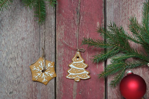Zwei Weihnachtsplätzchen hängen an einer roten Holzwand, Tannenzweige mit Weihnachtsschmuck — Stockfoto