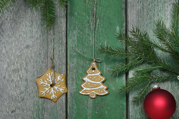 Weihnachtsplätzchen hängen an einer grünen Holzwand, Tannenzweige und festlicher Ball — Stockfoto