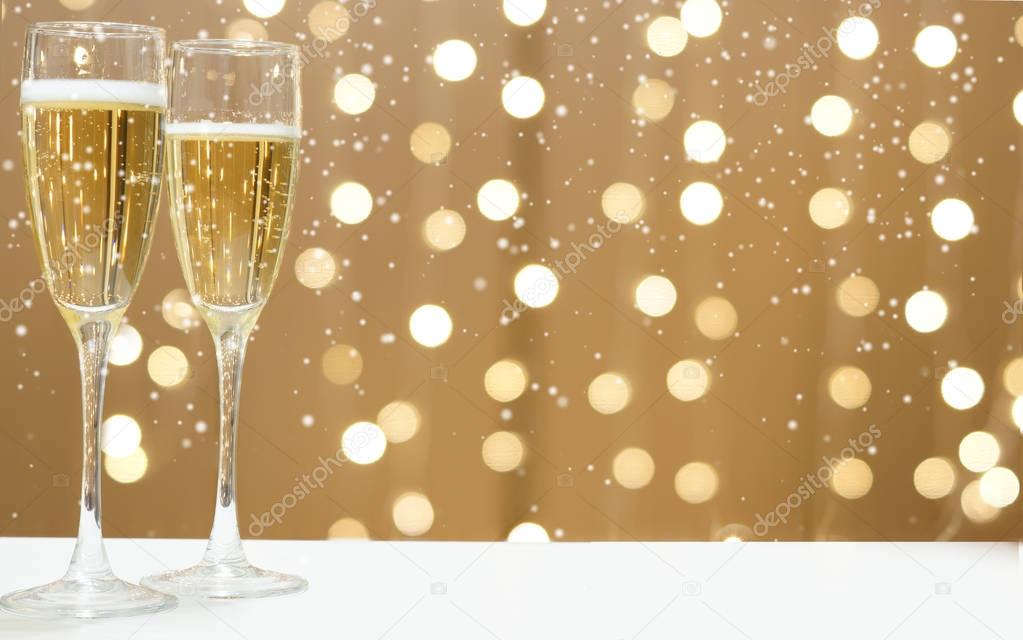 Two glasses of champagne against the festive garlands, white snow falls