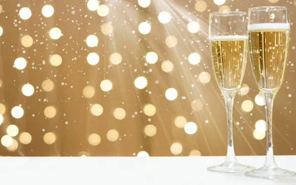 Two glasses of foaming champagne on the background of festive garlands, copy space for your text on the left