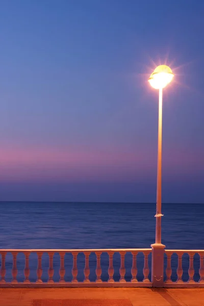 Leuchtende Laterne und Geländer der Böschung am Meer in der Morgendämmerung — Stockfoto