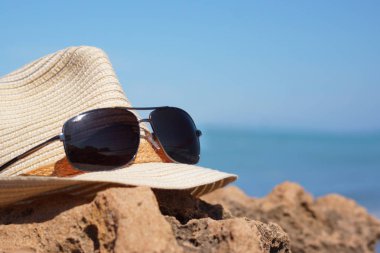 Güneş ve güneş gözlüğü yalan üzerine bir taş mavi denize yakın bir şapka