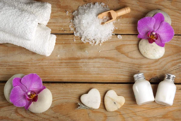 Spa situado en una mesa de madera con sal de baño blanco, loción, toallas y flores de orquídea sobre piedras —  Fotos de Stock