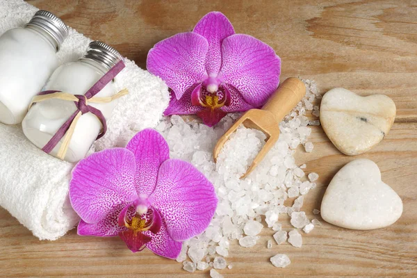 Комплект спа с белыми полотенцами, морской солью, деревянной лопаткой и ярким цветком орхидеи, камнями в форме сердец — стоковое фото