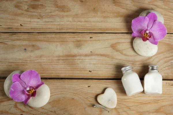 Bodylotion en stenen voor een hete massage zitten verspreid op een houten tafel voor spa behandeling. Sieraad van prachtige orchidee bloemen. — Stockfoto
