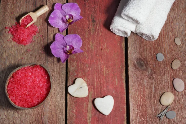 Spa posé sur des planches rouges avec des cœurs en pierre pour massage, sel de bain, serviettes et fleurs d'orchidée rose — Photo