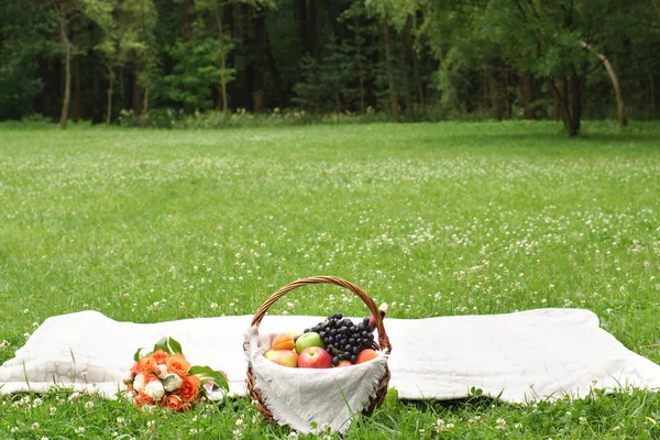 Summer picnic on a green glade with fruit and wine in a basket