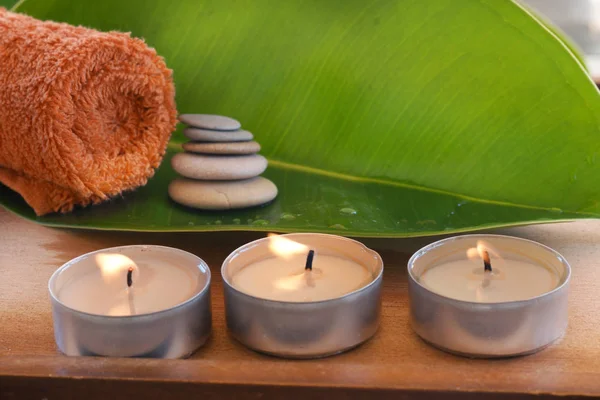 Brennende Kerzen neben einem Ficusblatt und einem orangefarbenen Handtuch — Stockfoto