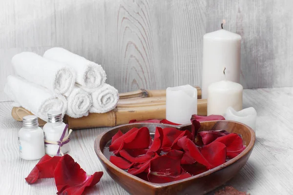 Pétales de rose rouge dans l'eau à côté d'un ensemble blanc pour les procédures de spa pour la peau des mains . — Photo