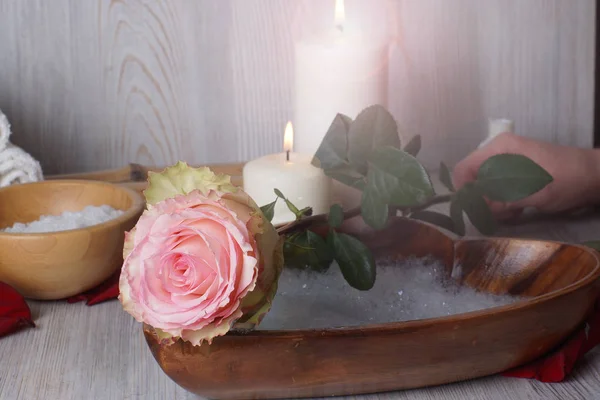 Uma mão feminina coloca uma rosa, uma preparação para um procedimento de spa para a pele das mãos . — Fotografia de Stock