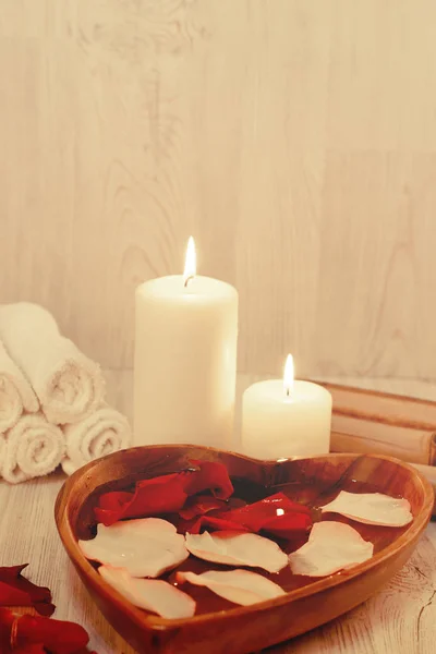 Tigela de madeira em forma de coração com pétalas de rosa e velas acesas nas proximidades, preparação para procedimentos de spa — Fotografia de Stock