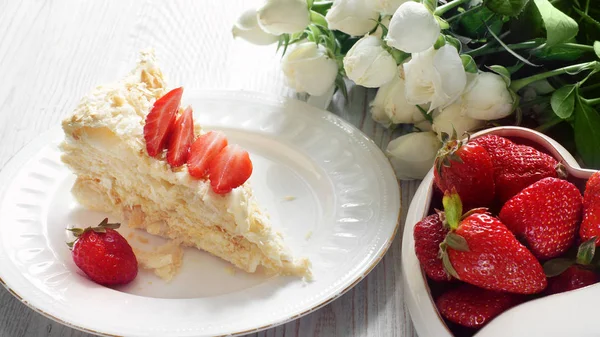 Un pedazo de pastel de Napoleón y un tazón en forma de corazón con una fresa roja, un ramo de flores al lado — Foto de Stock