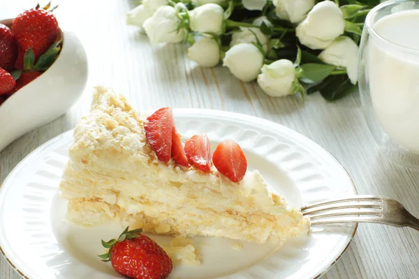 Un pedazo de pastel de Napoleón en un plato y un tazón de fresas, junto a un vaso de leche y un ramo — Foto de Stock