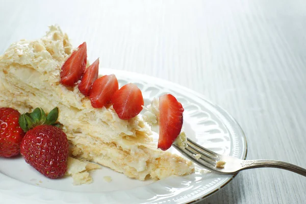 Un tenedor con un pedazo de pastel Napoleón en un plato decorado con una fresa roja madura — Foto de Stock
