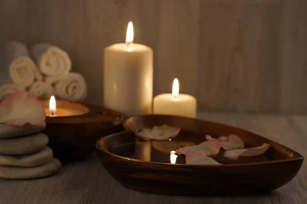 Burning white candles and spa treatment set, water with rose petals and towels — Stock Photo, Image