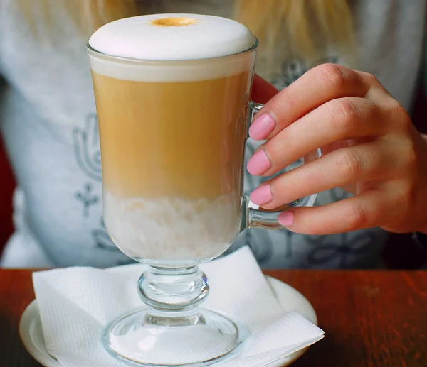 Elegant female hand hold a transparent cup with hot latte coffee in a cafe — Stock Photo, Image