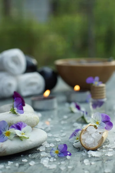 Łopata z solą do kąpieli i olejkiem do masażu na tle zestawu do zabiegów spa i płonących świec w ogrodzie letnim — Zdjęcie stockowe