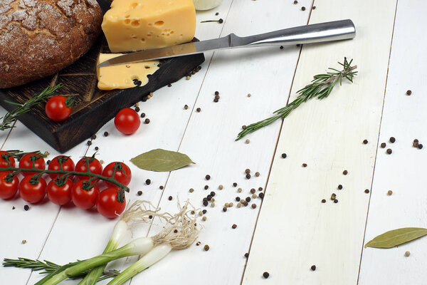 Rye bread, cheese, green onions and a sprig of cherry tomatoes lie on a board on a white wooden table
