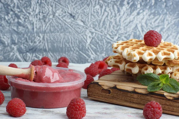 Miel batida rosa en un frasco con una cuchara de huso, jugosas frambuesas grandes y gofres dulces en la mesa — Foto de Stock